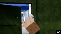 A worker wearing protective gear carries a box from an entrance gate to a pickup point outside a construction site at the Central Business District following the coronavirus outbreak in Beijing, March 2, 2020. 