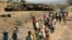 FILE - Villagers return from a market to Yechila town in south central Tigray walking past scores of burned vehicles, in Tigray, Ethiopia, July 10, 2021. 