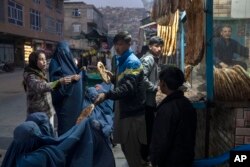 Seorang pria membagikan roti kepada perempuan Afghanistan yang mengenakan Burka di luar toko roti di Kabul, Afghanistan, Kamis, 2 Desember 2021. (Foto: AP)
