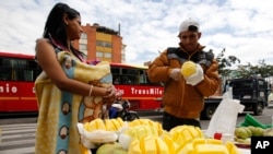 Saraid Valbuena, 20, holds her 4-month-old daughter bundled in a blanket, as her husband Jesus Barrios slices mangoes to sell, in Bogota, Colombia, June 9, 2017.