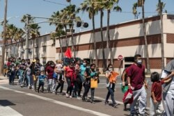 FILE - Asylum-seeking migrants walk to a temporary shelter run by a local charity organization after undergoing tests for COVID-19 in McAllen, Texas, April 8, 2021.