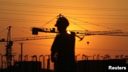 A worker walks with a hammer past a residential construction site during sunset in Nantong, Jiangsu province, China, Aug. 6, 2013. 