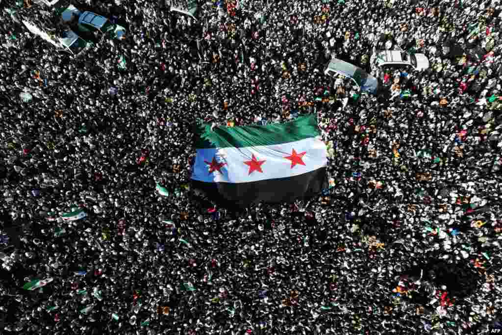 Crowds of Syrians raise a giant independence-era flag, used by the opposition since the uprising began in 2011, as they celebrate the fall of Bashar al-Assad&#39;s iron-fisted rule earlier this week, at the central Umayyad Square in Damascus.