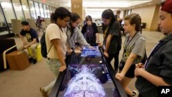 Teenagers look at the features of a virtual cadaver on the "Anatomage" table at the The University of Michigan Taubman Sciences Library in Ann Arbor, Michigan, May 20, 2016. 