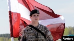 FILE - A Latvian soldier is seen holding a national flag as he waits to greet US soldiers arriving for exercises, at the airport in Riga April 24, 2014.
