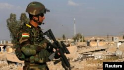 A Kurdish Peshmerga fighter walks past a house destroyed by American air strikes at Barznki village two days ago in Zummar, controlled by Islamic State (IS), near Mosul, Sept. 15, 2014. 