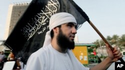Libyan follower of Ansar al-Shariah Brigades chants as he carries the Brigades flag, with Arabic writing that reads, "There is no God but Allah and Muhammad is his messenger, Ansar al-Shariah," during a protest in front of the Tibesti Hotel, in Benghazi, 