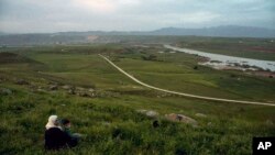 FILE - In this file photo dated Wednesday, May 1, 2019, a woman and child sit on a hill overlooking the Euphrates River as families picnic on May Day, in Derik, Syria. 