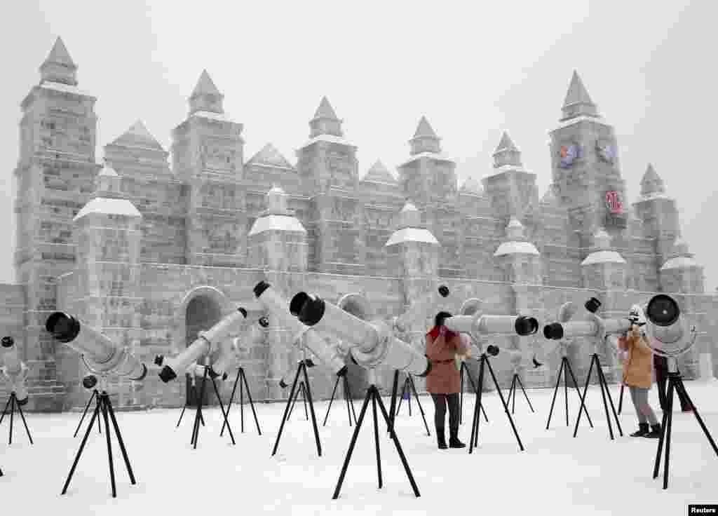 Pengunjung menggunakan kaleidoskop yang dipajang bersama patung es untuk Festival Es dan Salju Internasinal Harbin ke-31 di kota Harbin utara, provinsi province, China.