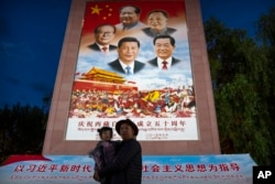 FILE - A man holds a girl as they pose for a photo in front of a large mural depicting Chinese President Xi Jinping, bottom center, and other Chinese leaders at a public square at the base of the Potala Palace in Lhasa in western China's Tibet Autonomous Region on June 1, 2021.