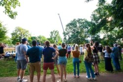 Onlookers watch as the monument of Confederate General Robert E. Lee is lifted from its pedestal, July 10, 2021, in Charlottesville, Va.