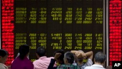 Para investor mengamati harga saham di lantai bursa Beijing, Jumat (21/8).