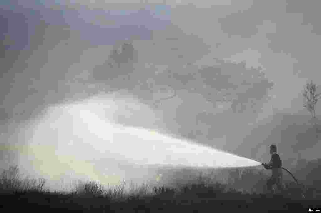 អ្នក​ពន្លត់អគ្គិភ័យ​ម្នាក់​បាញ់ទឹក​ពន្លត់ភ្លើង​នៅ​លើដី​ស្មៅ​មួយ​កន្លែង​នៅ​ទីក្រុង​ Carrwood ចក្រភពអង់គ្លេស។