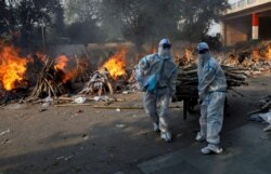 Health workers wearing personal protective equipment (PPE) carry wood to prepare a funeral pyre for a coronavirus victim during a mass cremation at a crematorium in New Delhi, India, April 26, 2021.