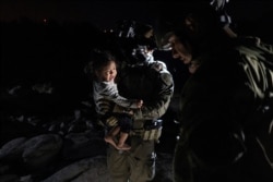 An asylum-seeking migrant girl is carried by a Department of Public Safety agent while her mother is disembarking from an inflatable raft after crossing the Rio Grande river into the United States from Mexico in Roma, Texas, May 5, 2021.