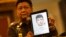 Police spokesman Lt. Gen. Prawuth Thavornsiri shows a photo of one of three men that Thai authorities have issued new arrest warrants in connection with the bombing case, bringing the total number of wanted suspects to seven during a press conference in Bangkok, Thailand, Tuesday, Sept. 1, 2015. Thai authorities arrested a man they believe is part of a group responsible for a deadly bombing at a shrine in central Bangkok two weeks ago, Prime Minister Prayuth Chan-ocha announced Tuesday. He said the suspect resembles a yellow-shirted man in a surveillance video who police say planted the bomb. (AP Photo/Sakchai Lalit) 