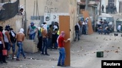 A masked Palestinian hides behind a plank of wood during clashes in the East Jerusalem neighborhood of Wadi al-Joz, Sept. 7, 2014. 