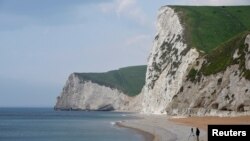 FILE - A man takes photographs pointing south on the beach at Durdle Door with the English Channel sea connecting Britain to mainland Europe seen behind, in southwest England, May 13, 2016. 