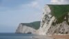FILE - A man takes photographs pointing south on the beach at Durdle Door with the English Channel sea connecting Britain to mainland Europe seen behind, in south west England, May 13, 2016. 
