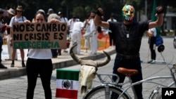 A woman holds a sign that reads in Spanish "It is not change, or crisis. It's an emergency" as she stands next to another demonstrator with a bicycle during a global protest on climate change in Mexico City, Sept. 20, 2019.