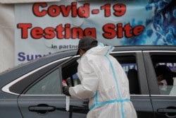A healthcare worker takes a swab from a person sitting in a car at a drive-thru COVID-19 test center in Newark, New Jersey, Nov. 12, 2020.