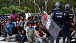 FILE - Migrants sit on the ground next to Spanish police officers after storming a fence to enter the Spanish enclave of Ceuta, Spain, Feb. 17, 2017.