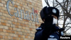 在加拿大驻北京大使馆外一名中国警察向摄影记者打手势。（2018年12月12日）