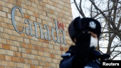 Seorang polisi memberi isyarat kepada para fotografer di luar Kedutaan Besar Kanada di Beijing, China, 12 Desember 2018. 