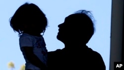 In this April 22, 2020, photo, Afghan refugee Mahmood Amiri carries his daughter, Safa, in West Valley City, Utah. The coronavirus restrictions imposed across the U.S. have affected refugee families in many of the same ways as other Americans, but many of