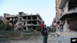 FILE - A civilian fighter holding the Libyan flag stands in front of damaged buildings in Benghazi, Libya, Feb. 23, 2016.