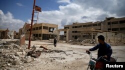FILE - A man rides on a motorbike as another one walks past damaged buildings in the rebel-controlled area of al-Nashabyia town in Eastern Ghouta, Syria, April 13, 2016. 