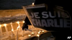A woman holding a sign that read in French "I am Charlie" lights a candle during a demonstration in solidarity with those killed in an attack at the Paris offices of the weekly newspaper Charlie Hebdo in Kosovo capital Pristina, Jan. 7, 2015. 