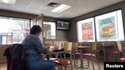 A woman eats in a fast food restaurant as a television shows live coverage of U.S. President Donald Trump's U.S. Senate impeachment trial three days before the Iowa caucus in Des Moines, Iowa, Jan. 31, 2020.