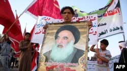Seorang pria Irak membawa poster bergambar Ulama Syiah Ayatollah Ali al-Sistani saat berkumpul untuk bergabung dengan pasukan keamanan Irak untuk melawan militan (19/6). (AFP/Haidar Mohammed Ali)