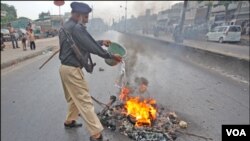 Seorang polisi Pakistan berusaha memadamkan api dalam kerusuhan di Karachi (1/8).