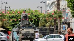 Tunisians walk past a military armored personnel carrier at Habib Bourguiba Avenue July 30, 2021. 