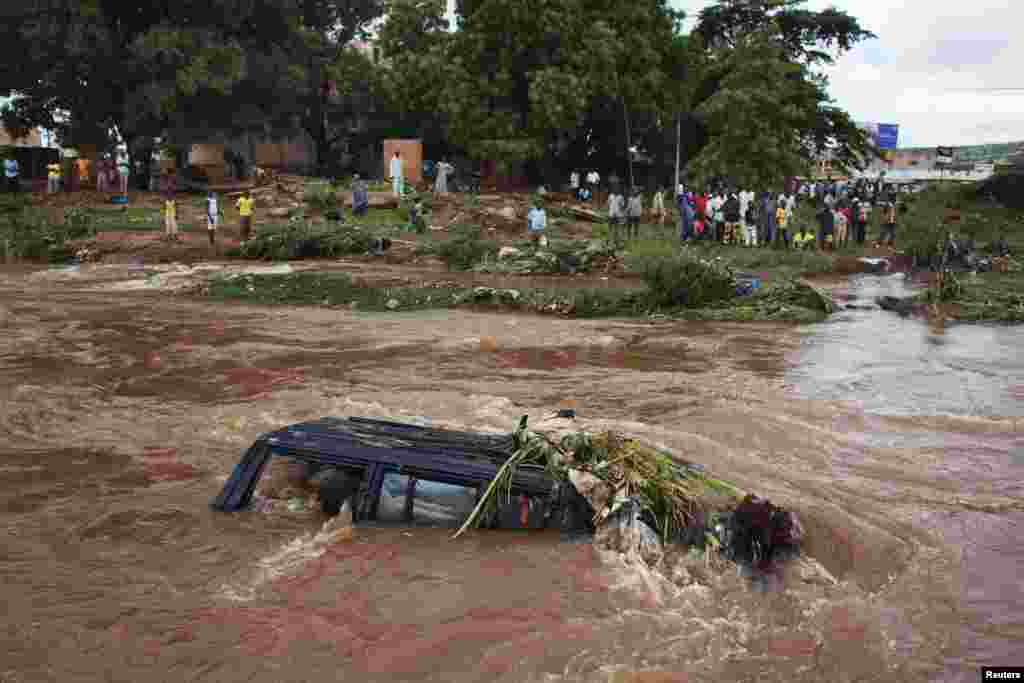 Warga menyaksikan sebuah kendaraan terendam banjir di Bamako, Mali. Hujan deras menyebabkan banjir bandang, menggenangi rumah di berbagai daerah.