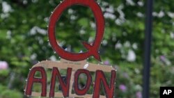 FILE - In this May 14, 2020, file photo, a person carries a sign supporting QAnon at a protest rally in Olympia, Wash. Facebook said Tuesday, Oct. 6, 2020, that it will remove Facebook pages, groups and Instagram accounts for “representing QAnon.” (AP Photo/Ted S. Warren, File)