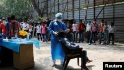 A healthcare worker wearing personal protective equipment (PPE) takes a swab from a migrant laborer for a rapid antigen test at the site of an under construction residential complex in New Delhi, India, Sept. 19, 2020.