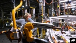 FILE - GM workers use human assistance automation to weld vehicle doors at the General Motors assembly plant during the COVID-19 pandemic in Oshawa, Ontario, March 19, 2021.