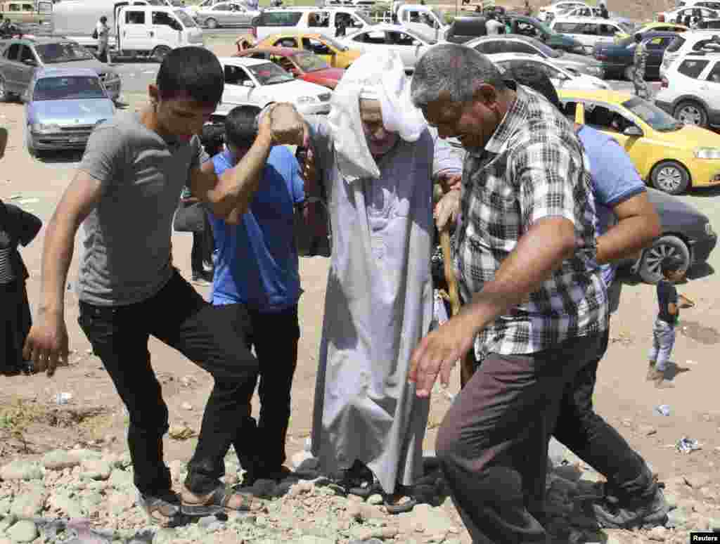 An elderly man is assisted as families fleeing the violence in Mosul wait at a checkpoint on the outskirts of Irbil, Iraq, June 10, 2014. 