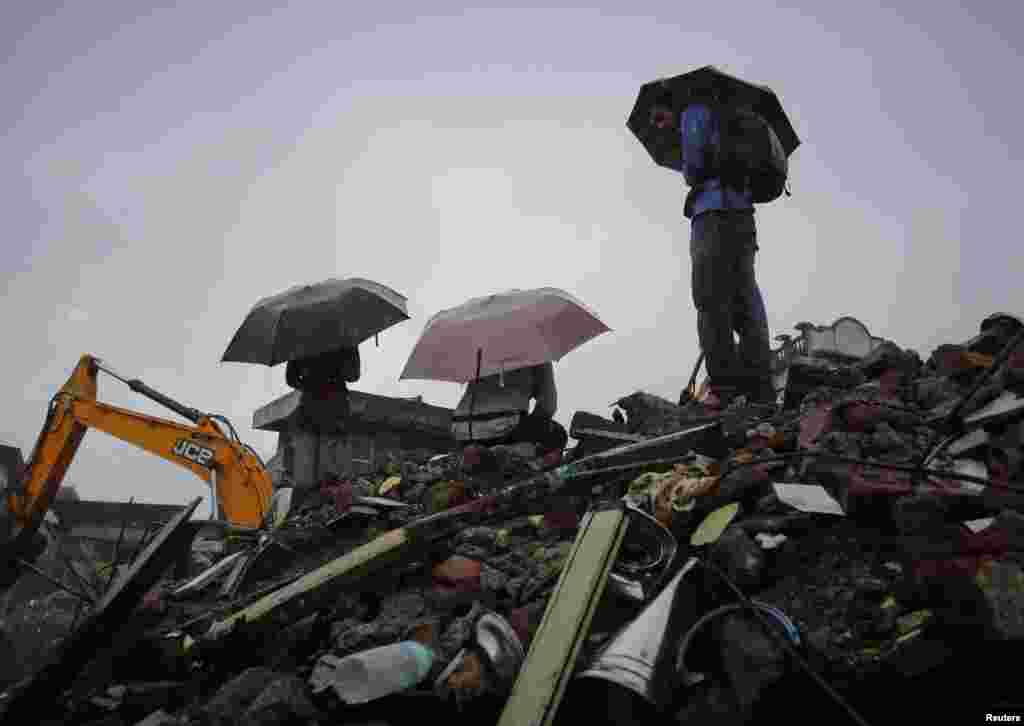 People holding umbrellas gather in the rain on the rubble of a collapsed residential building on the outskirts of Mumbai, India, June 21, 2013.
