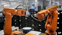 FILE - A Chinese worker is seen behind orange robot arms at work at Rapoo Technology factory in southern Chinese city of Shenzhen.