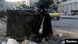 FILE - A woman is seen searching for food in a garbage container in Aleppo, Syria, July 31, 2013.