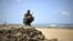 A handout picture released by the African Union-United Nations Information Support Team shows an armed man squatting at a beach during a demonstration by a local militia, formed in order to provide security in the town of Marka, April 30, 2014.