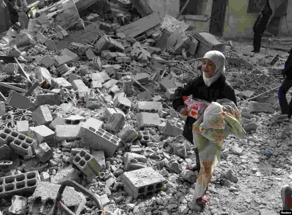 A girl carries her belongings as she walks on rubble at a site hit by what activists said was an airstrike by forces loyal to Syria's President Bashar al-Assad in Arbeen, Jan. 14, 2014.
