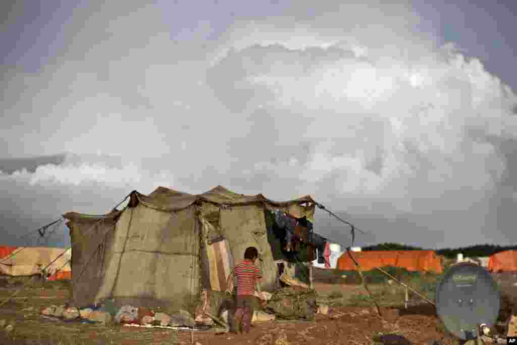 A Syrian refugee boy carries his muddy shoes heading back to his tent following rainfall at an informal tented settlement near the Syrian border on the outskirts of Mafraq, Jordan.