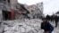 FILE - People walk past debris following airstrikes by government forces, in the town of Ariha, Idlib province, Syria, Jan. 15, 2020. 