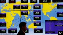 A man walks past a bank's electronic board showing the share indexes around the world at the Hong Kong Stock Exchange, Aug. 27, 2015.