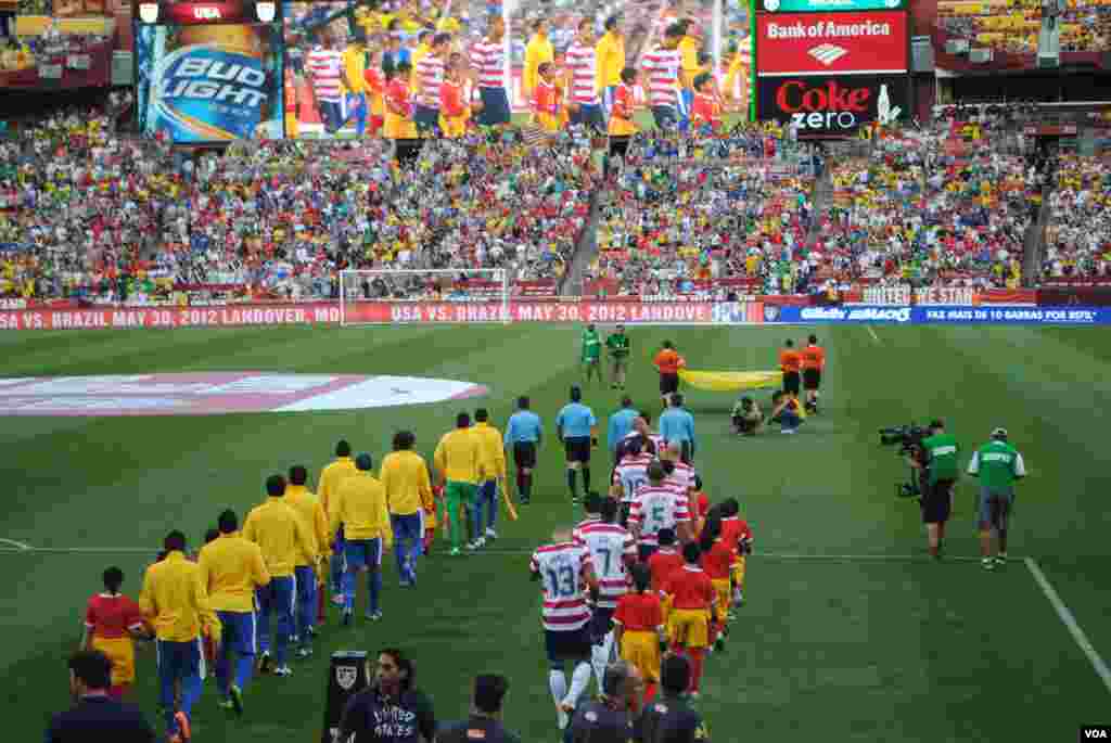 Brazilian and U.S. team members march onto the field for the national anthems. VOA/M. Lipin